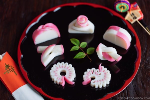 Decorative kamaboko fish cakes on a black and red lacquered board.