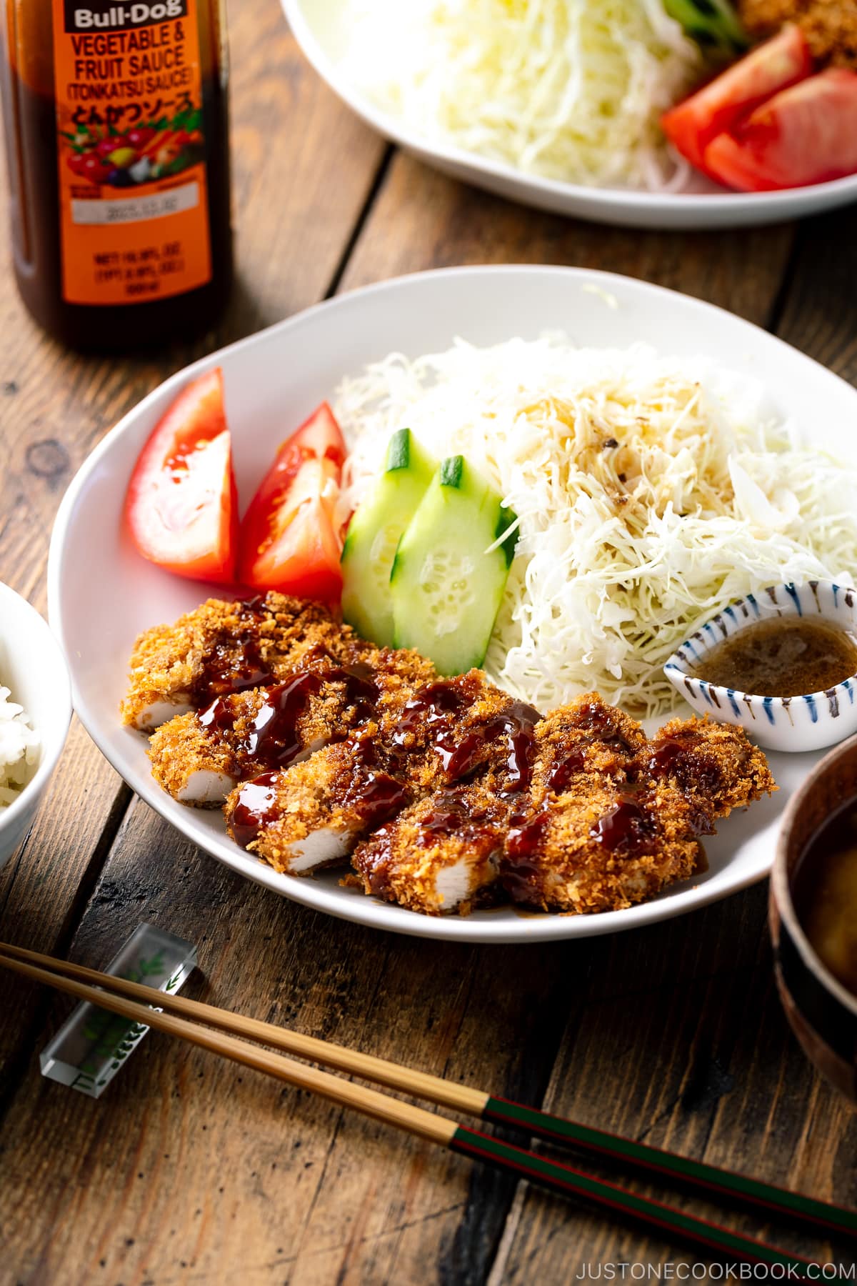 A white plate containing Baked Chicken Katsu (Japanese Chicken Cutlets) and shredded cabbage salad.