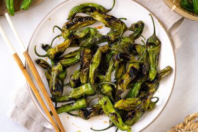 A white plate containing Blistered Shishito Peppers With Ginger Soy Sauce.