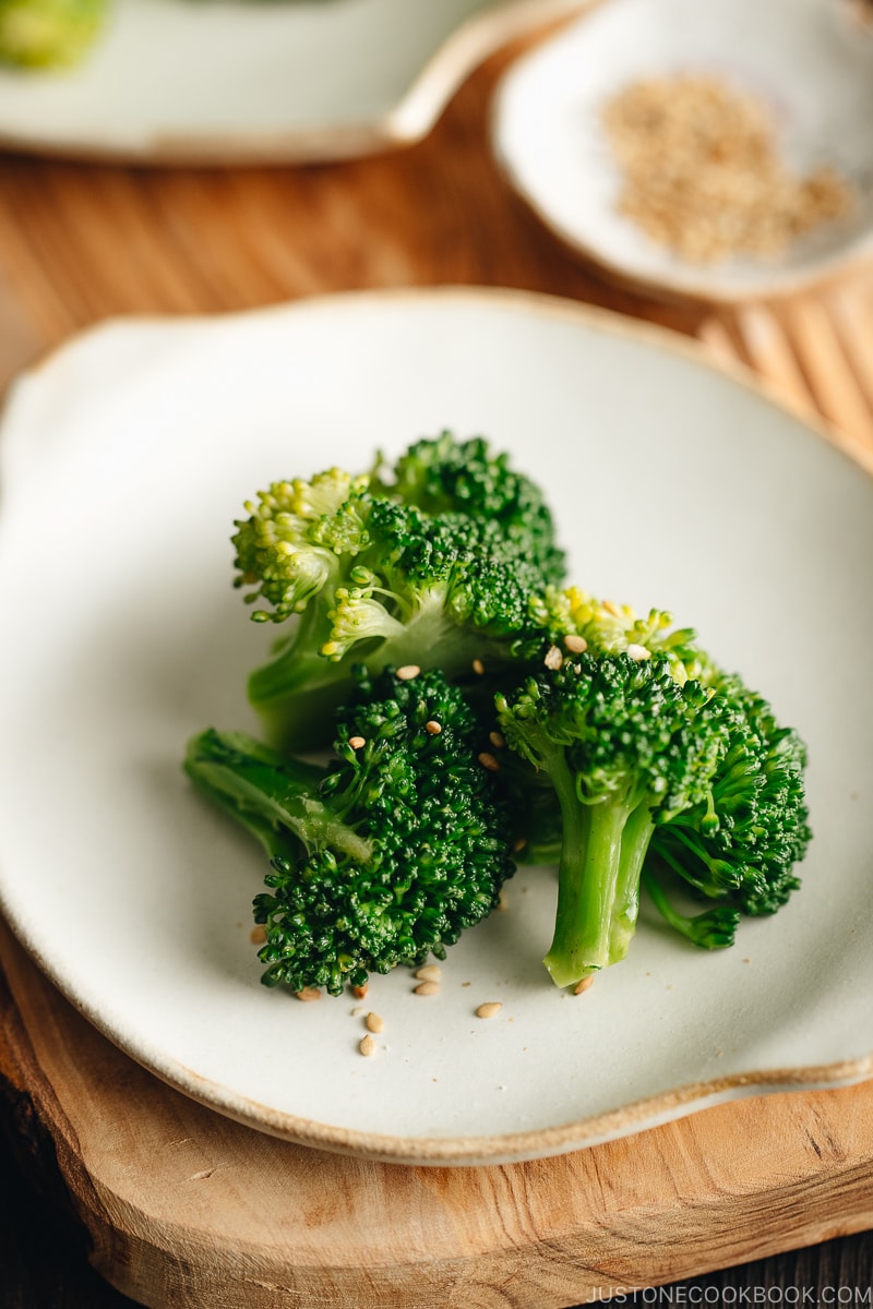 A white plate containing blanched broccoli tossed with sesame seeds.