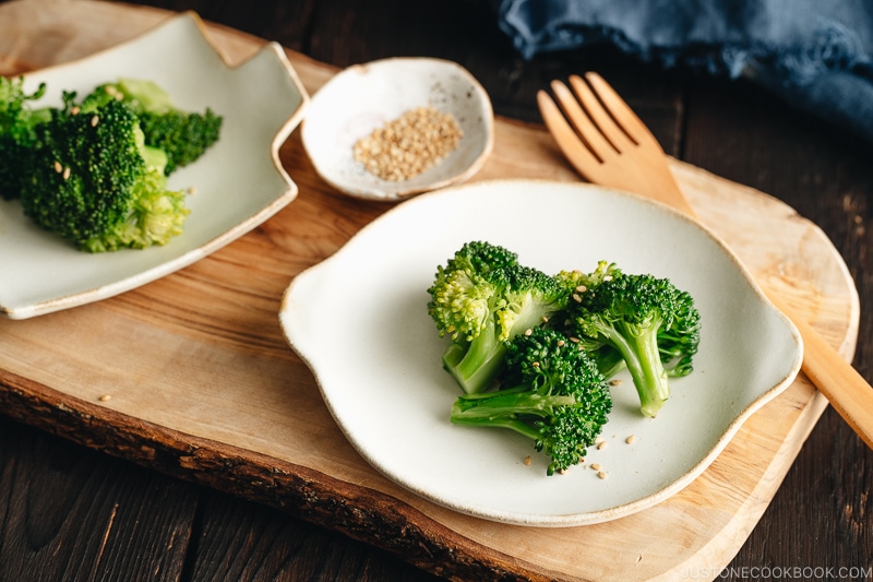 A white plate containing blanched broccoli tossed with sesame seeds.