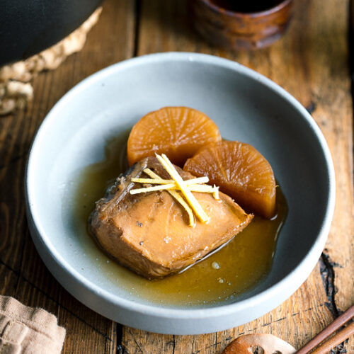 A grey bowl containing buri daikon, a simmered yellowtail and daikon radish, garnished with julienned ginger.