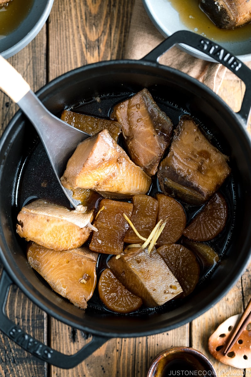 A grey bowl containing buri daikon, a simmered yellowtail and daikon radish, garnished with julienned ginger.