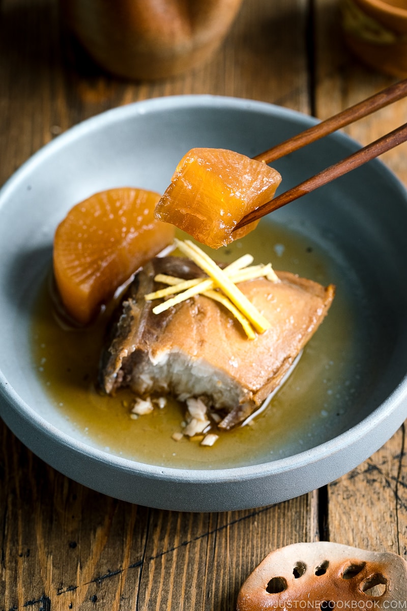 A grey bowl containing buri daikon, a simmered yellowtail and daikon radish, garnished with julienned ginger.