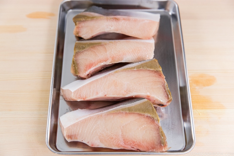 four pieces of hamachi on a metal tray