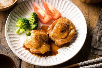 A plate containing butter shoyu chicken, broccoli, and tomatoes.