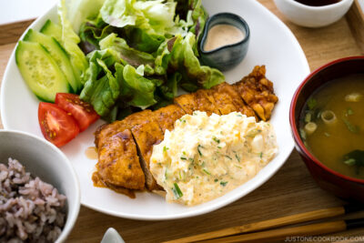 A white plate containing crispy chicken dressed with a tangy sauce and served with homemade tartar sauce.