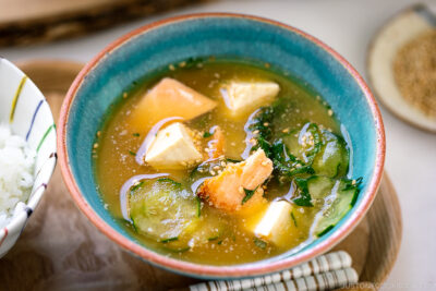 A cobalt blue ceramic bowl containing cold miso soup (hiyajiru) with tofu, cucumber, and salmon).