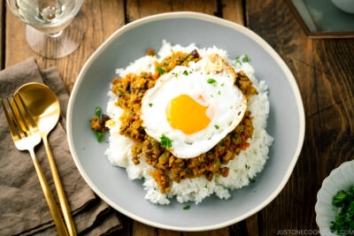 A ceramic plate containing steamed rice, dry curry, and a fried egg.