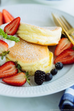 A white plate containing fluffy Japanese souffle pancakes, fresh berries, and whipped cream.