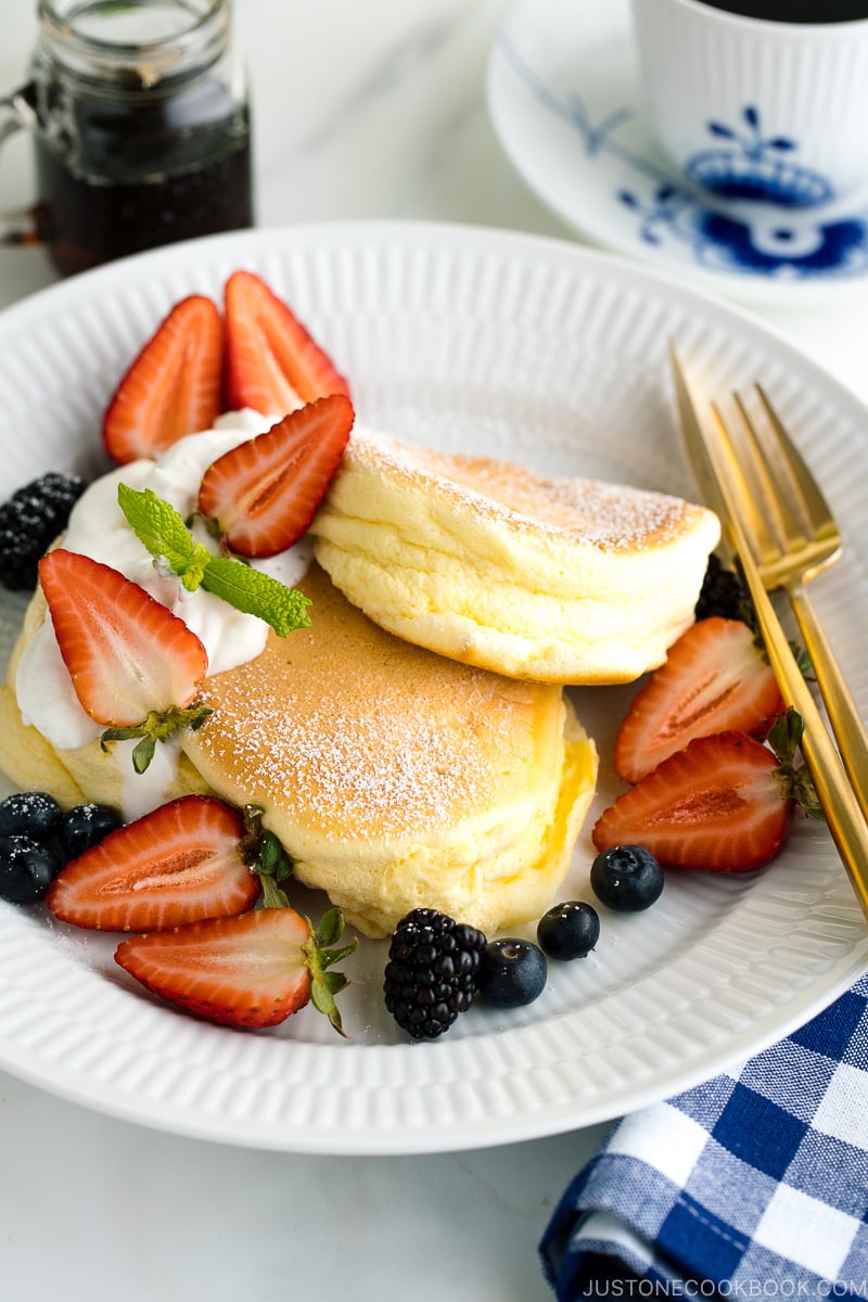 A white plate containing fluffy Japanese souffle pancakes, fresh berries, and whipped cream.