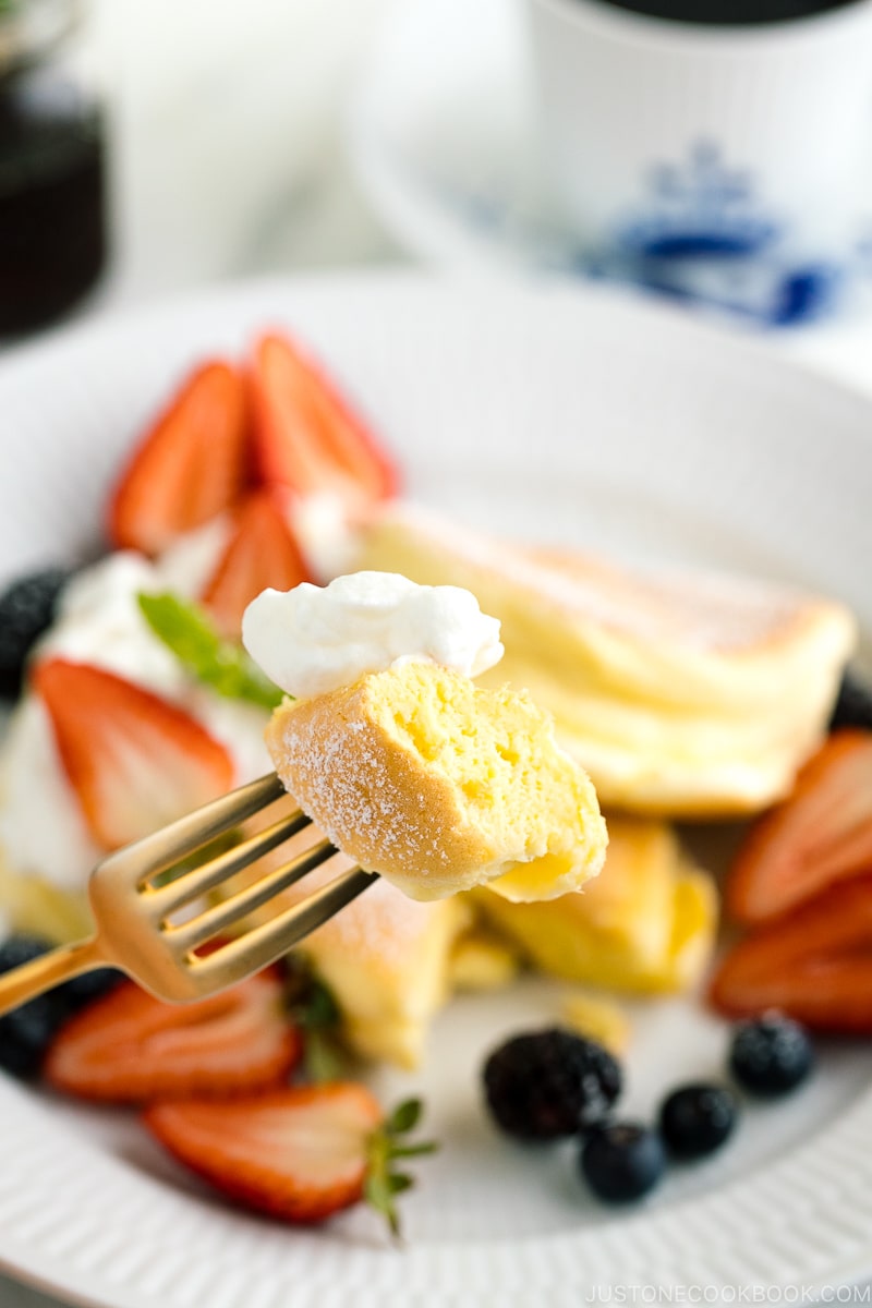 A white plate containing fluffy Japanese souffle pancakes, fresh berries, and whipped cream.