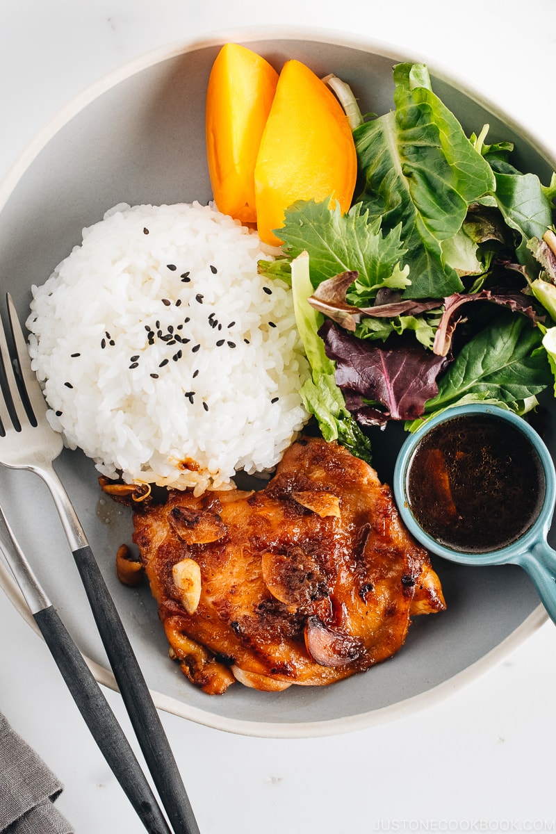 A large gray plate containing garlic onion chicken, green leaf salad, and steamed rice.