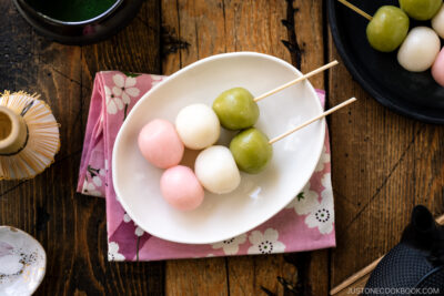 A white oval plate containing two Hanami Dango, served with matcha green tea.