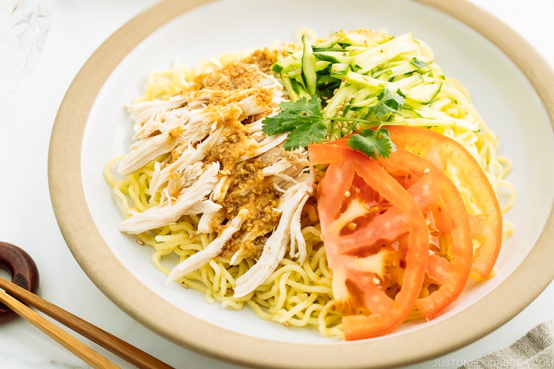 A ceramic plate containing Hiyashi Chuka (Cold Ramen) with Sesame Miso Sauce. Chilled noodles are served with sliced tomatoes, shredded chicken, and cucumber.