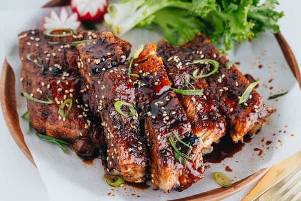 Sticky Asian Ribs on a white platter, topped with sprinkle of green onion.