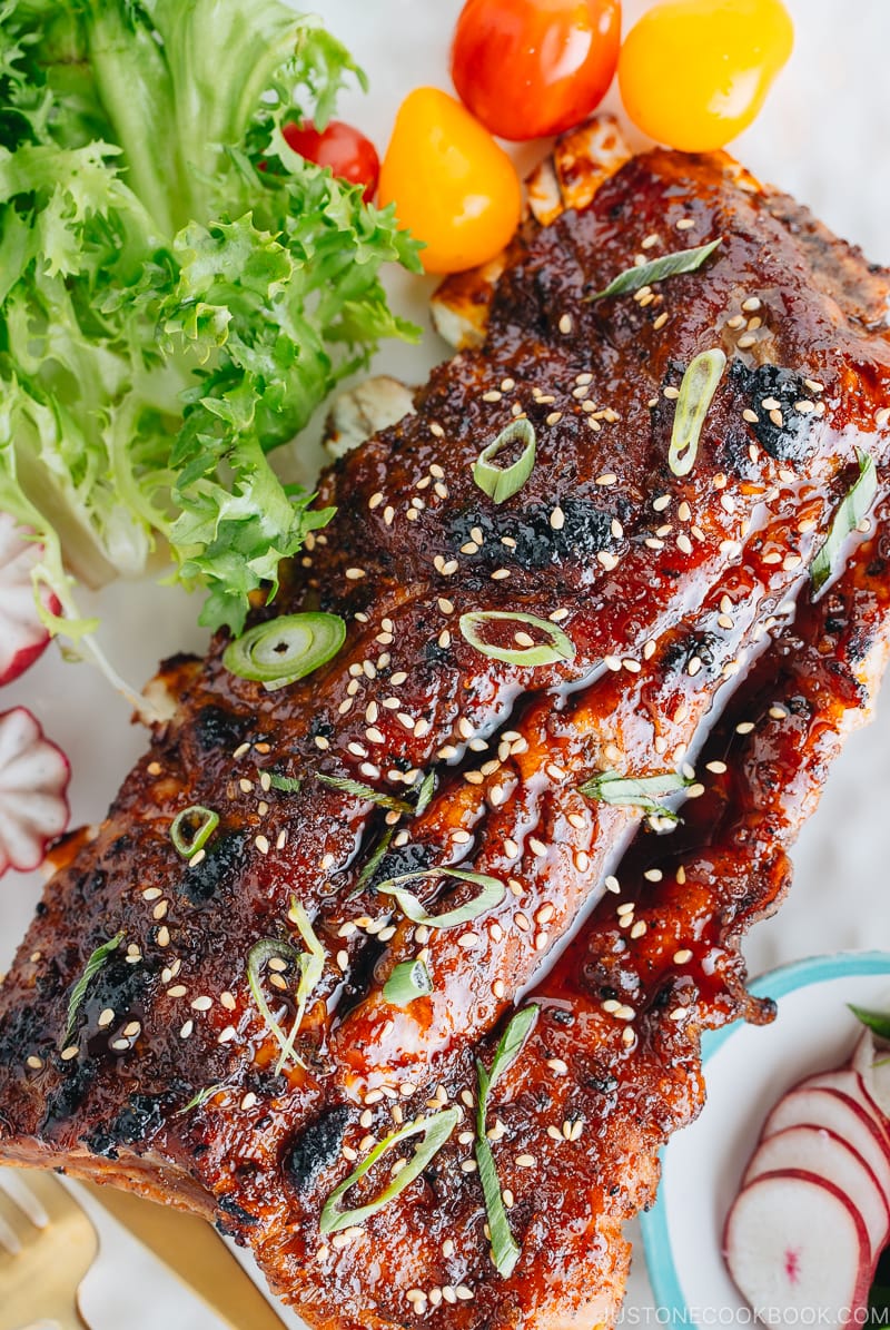 Sticky Asian Ribs on a white platter, topped with sprinkle of green onion.