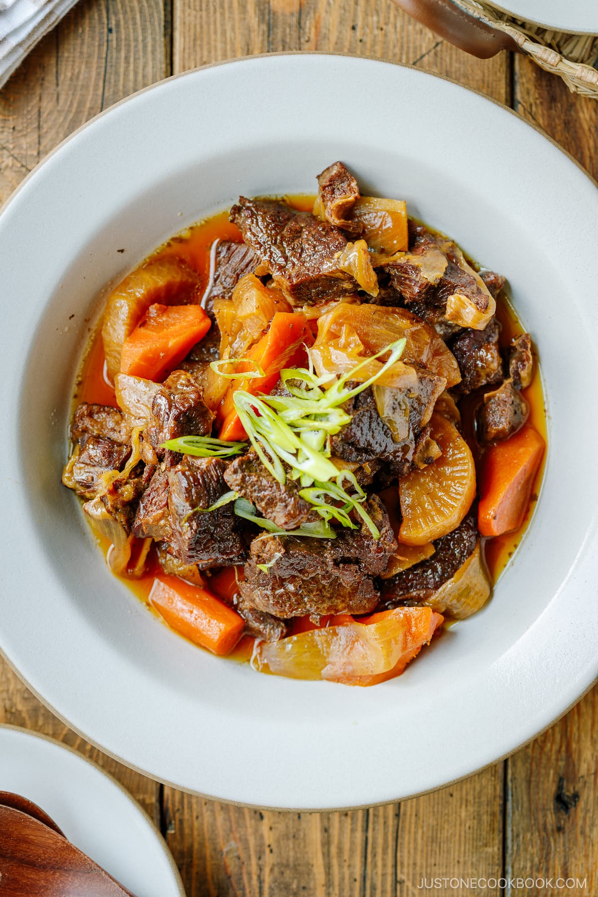 A white ceramic bowl containing Instant Pot Short Ribs with daikon and carrots pressure cooked in a savory sauce.