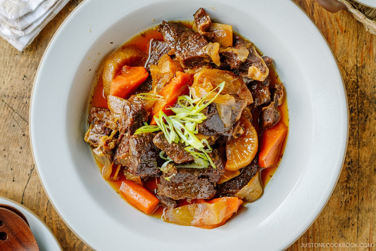 A white ceramic bowl containing Instant Pot Short Ribs with daikon and carrots pressure cooked in a savory sauce.