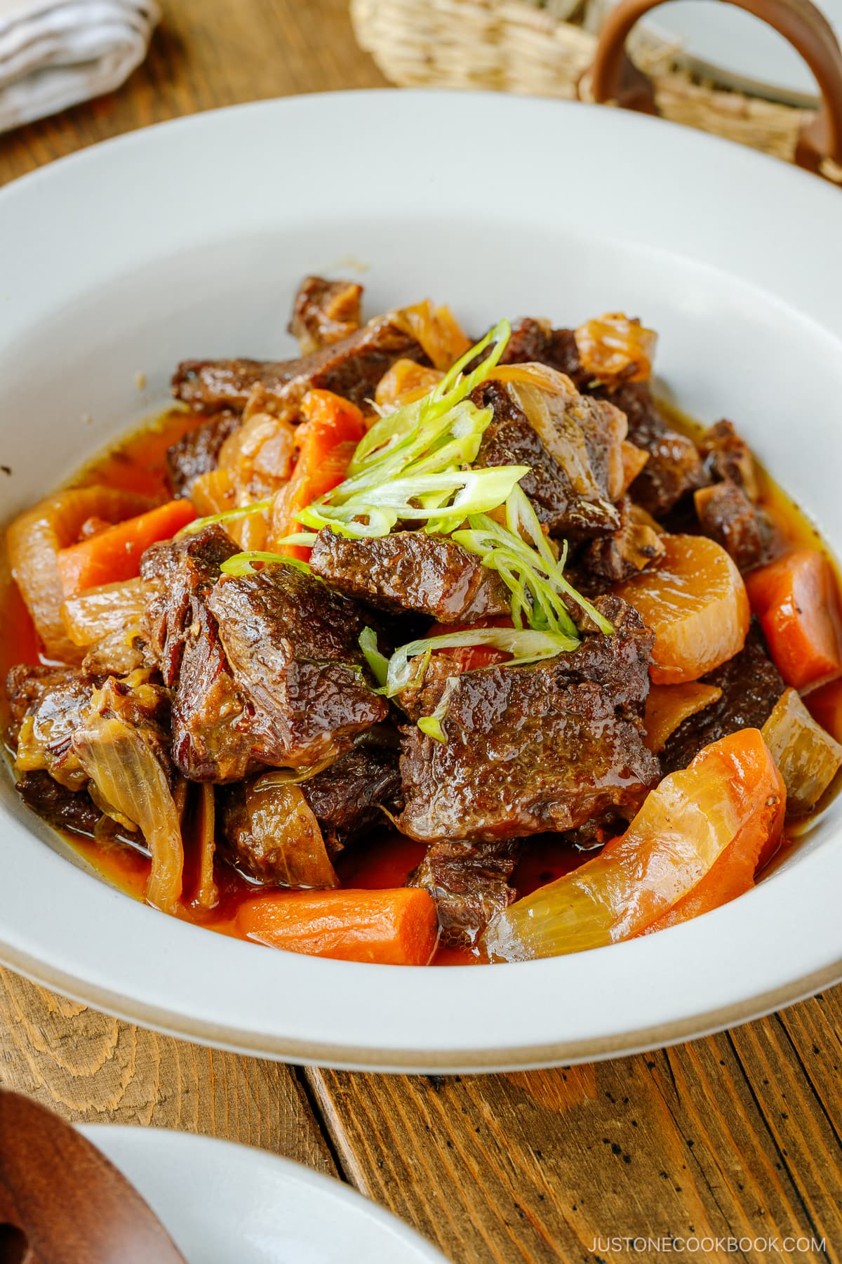 A white ceramic bowl containing Instant Pot Short Ribs with daikon and carrots pressure cooked in a savory sauce.