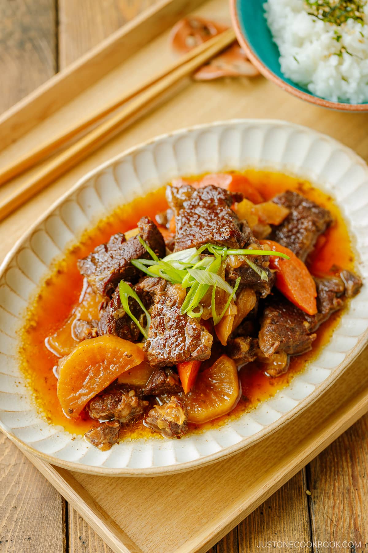 A white ceramic bowl containing Instant Pot Short Ribs with daikon and carrots pressure cooked in a savory sauce.