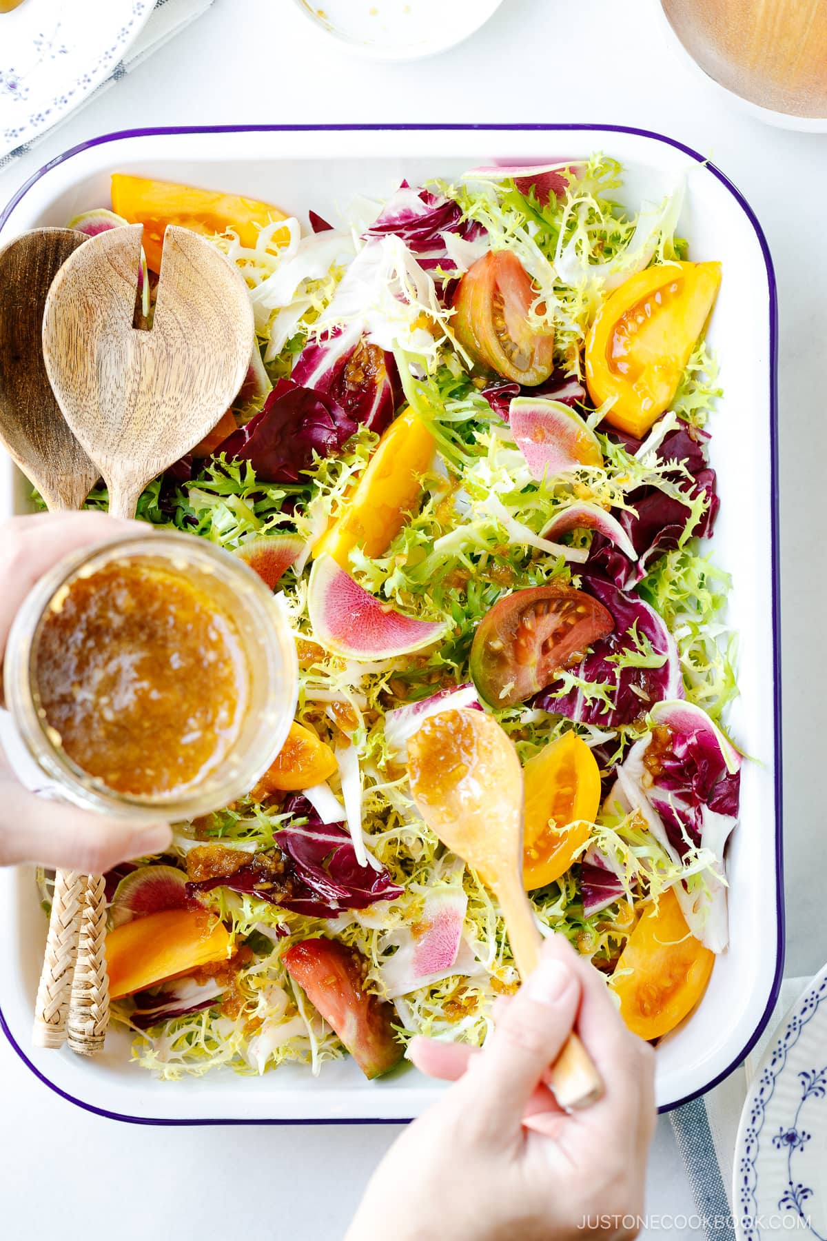 A white and blue enamel tray containing frisee and radicchio lettuce, thinly sliced watermelon radish, and heirloom tomatoes, drizzled with Japanese onion dressing.