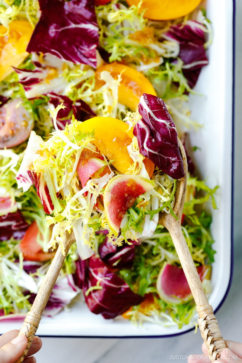 A white and blue enamel tray containing frisee and radicchio lettuce, thinly sliced watermelon radish, and heirloom tomatoes, drizzled with Japanese onion dressing.