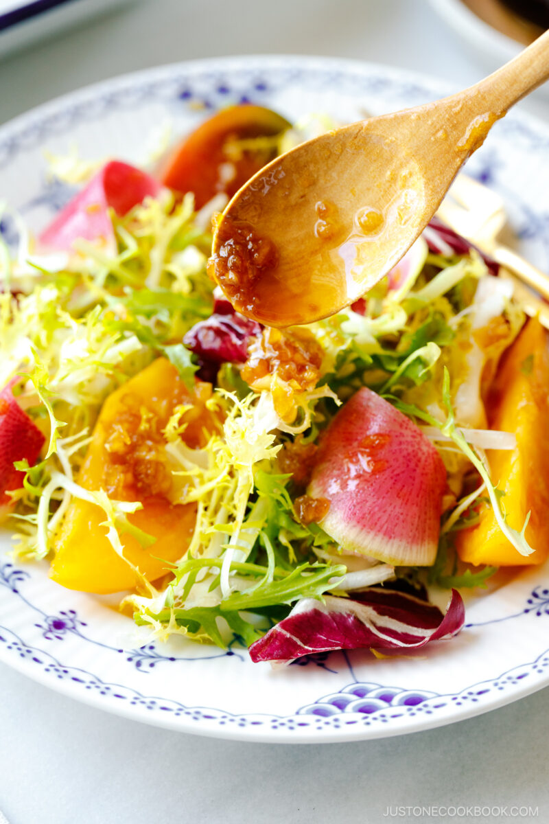 A white and blue plate containing frisee and radicchio lettuce, thinly sliced watermelon radish, and heirloom tomatoes, drizzled with Japanese onion dressing.