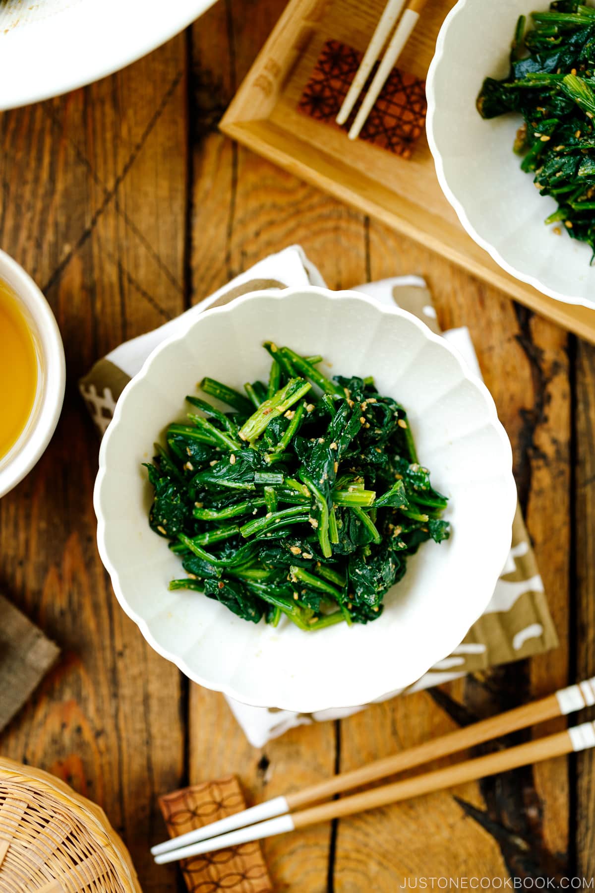 A white fluted dish containing Japanese spinach salad seasoned with sesame seeds, soy sauce, and sugar.