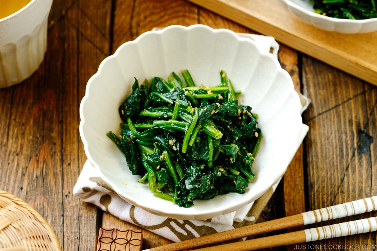 A white fluted dish containing Japanese spinach salad seasoned with sesame seeds, soy sauce, and sugar.