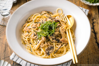 A white ceramic plate containing Japanese-style Tuna Mushroom Pasta garnished with shredded nori and shiso leaves.