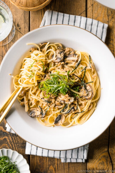 A white ceramic plate containing Japanese-style Tuna Mushroom Pasta garnished with shredded nori and shiso leaves.