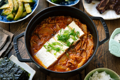 A black staub containing Kimchi Jjigae (Stew) topped with slices of tofu.