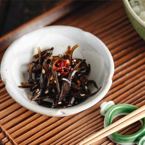 Simmered kombu in a small dish next to a bowl of steamed rice.