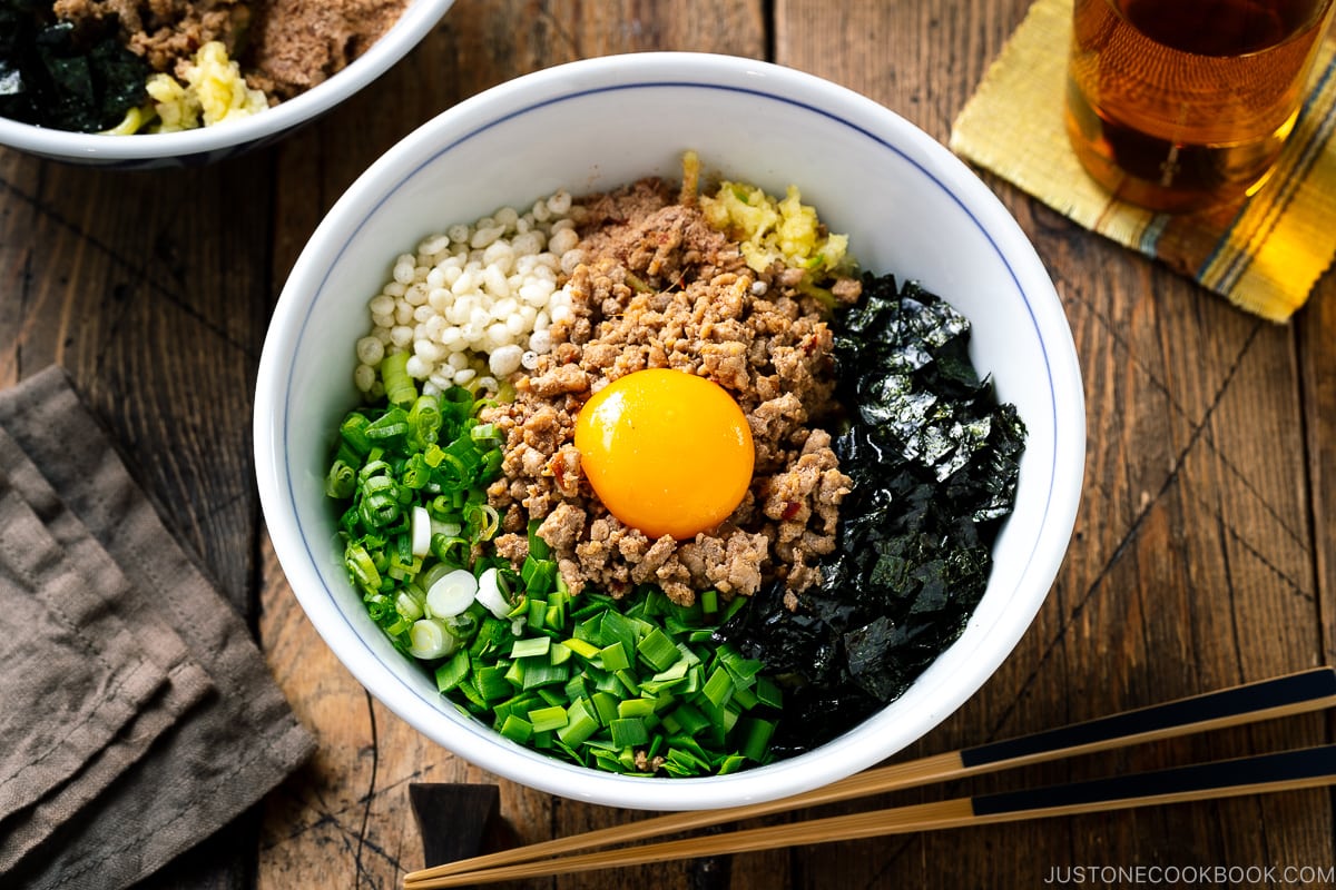 A bowl containing Mazesoba (Mazemen), Japanese Brothless Ramen, topped with seasoned minced meat, green onion, garlic chives, nori seaweed, crushed garlic, and katsuobushi powder.