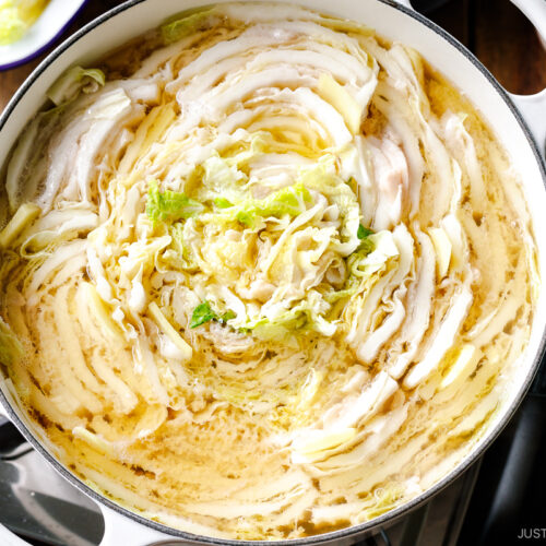 A Le Creuset pot containing Mille-Feuille Nabe, which is a hot pot dish with layers of pork belly slices and napa cabbage slices in a dashi broth.