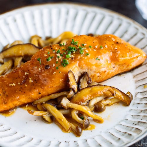 A white plate containing Miso Butter Salmon served with sautéed shiitake and shimeji mushrooms.