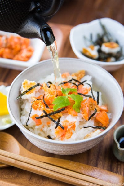 Japanese tea is poured on top of steamed rice and flaky baked salmon in a rice bowl.