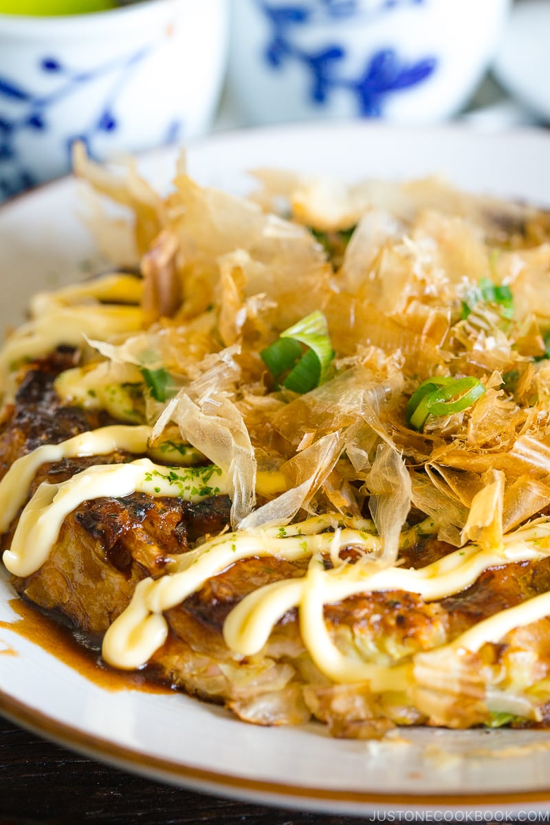 A white plate containing Okonomiyaki, Japanese savory pancake.