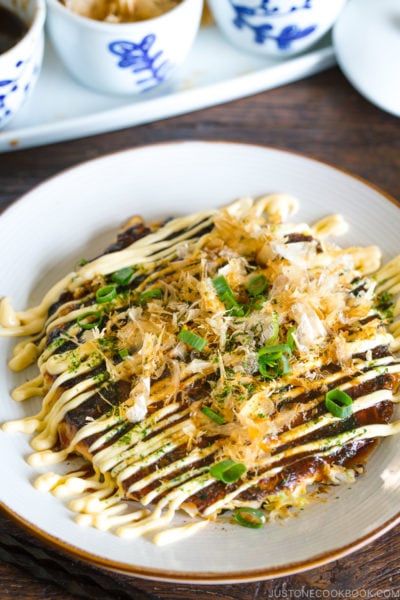 A white plate containing Okonomiyaki, Japanese savory pancake.