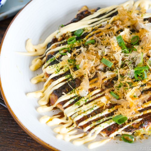 A white plate containing Okonomiyaki, Japanese savory pancake.