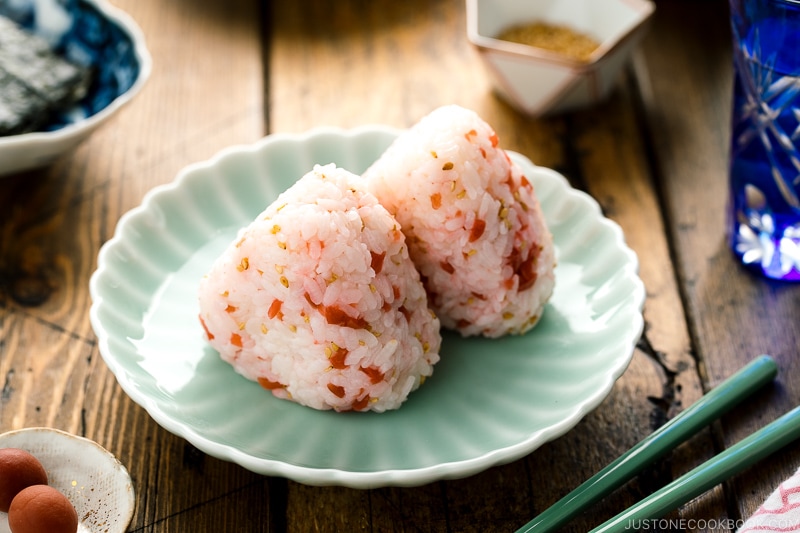 Plum rice balls on a light green plate served with nori seaweed.