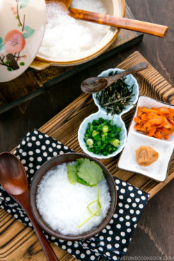 Japanese rice porridge served in a bowl with salmon, green onion, pickled plums, and shredded seaweed.