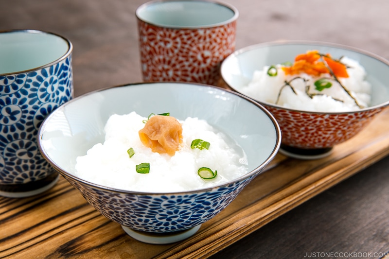 Japanese rice porridge served in a bowl with salmon, green onion, pickled plums, and shredded seaweed.