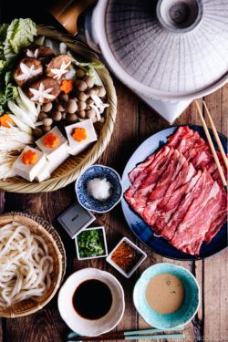 Tablesetup for shabu shabu - donabe hot pot, vegetables, meat, udon, and dipping sauces.