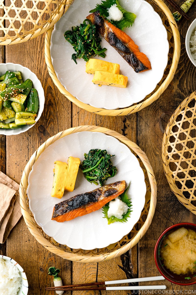 A white plate containing Japanese salted salmon (Shiozake), tamagoyaki, and spinach salad.