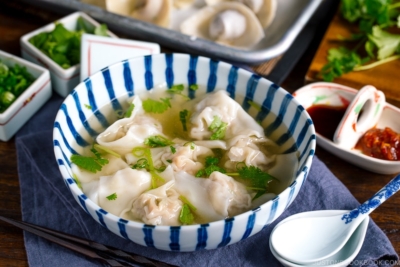 a large bowl containing shrimp and wonton soup along with the condiments.