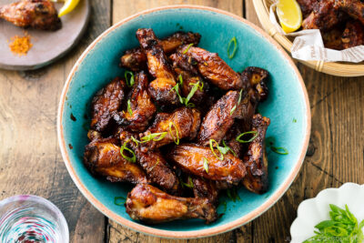 A blue ceramic bowl containing Smoked Chicken Wings with Sweet-Salty Japanese Sauce sprinkled with scallions.