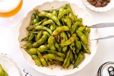 A white ceramic plate containing spicy edamame.