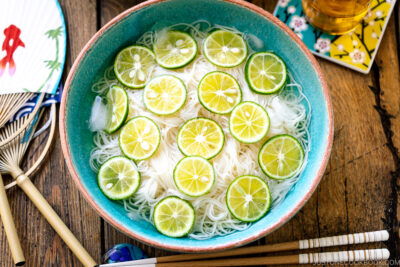 A blue bowl containing cold somen noodles topped with thinly sliced sudachi citrus.